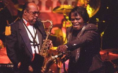 James Brown performs on stage beside his saxophonist.