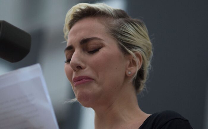 Lady Gaga sheds a tear as she speaks at the microphone.