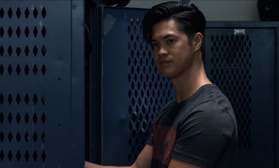 Ross Butler is standing in front of his football locker with his hand inside. 