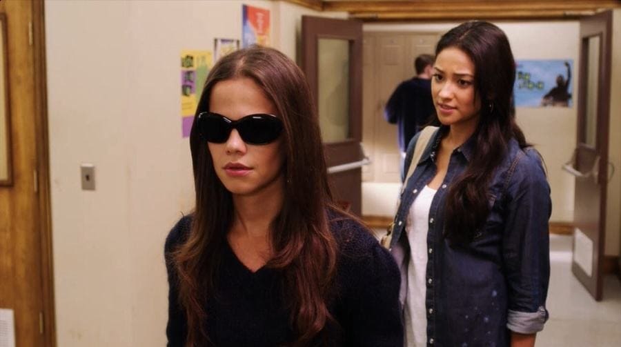 Tammin Sursok with dark sunglasses on, and Shay Mitchell is standing in the high school hallway for the show. 