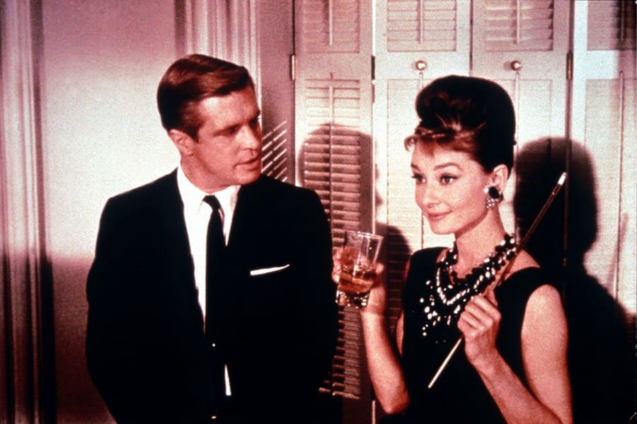 Audrey Hepburn and George Peppard are standing around at a party in the movie Breakfast at Tiffany’s. 