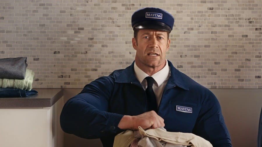 Colin Ferguson holding laundry in a navy blue Maytag uniform.