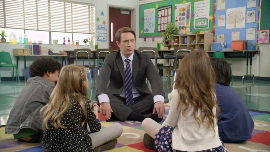Beck Bennett sitting in a circle with kids in a classroom.