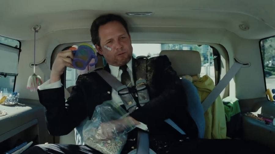 Dean Winters in the back seat of a minivan eating lucky charms and drinking from a sippy cup.