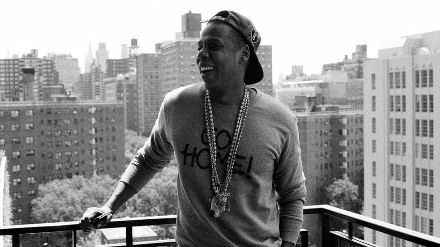 Jay Z standing on a porch with a nice building view behind him.