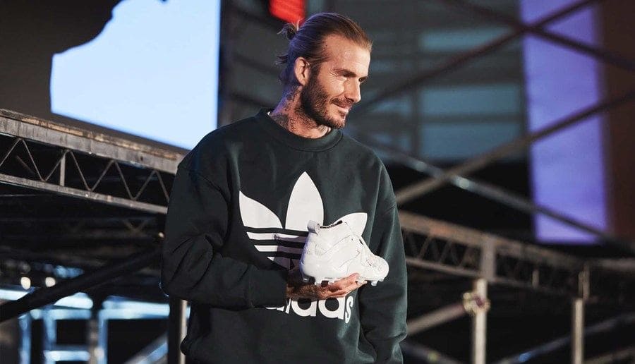 David Beckham holding an Adidas soccer shoe and wearing an Adidas sweater.