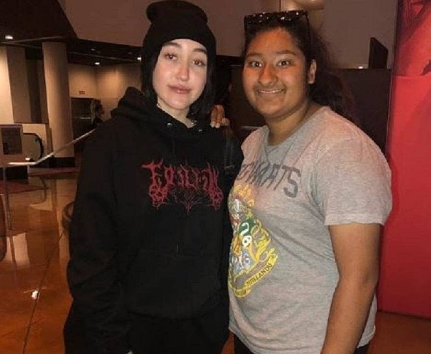 Noah Cyrus is posing with Marlen Orozco for a photograph in an empty shopping center.