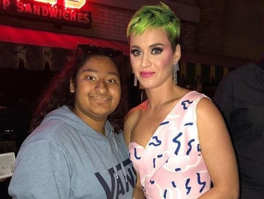Marlen and Katy Perry are standing in front of a sandwich shop with neon lights on.