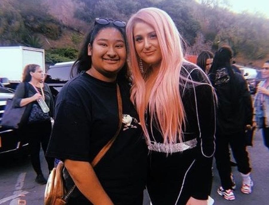 Marlen and Meghan Trainor are standing in a parking lot, posing for a photograph.