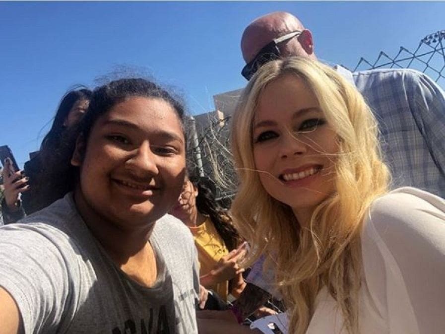 A selfie of Avril Lavigne and Marlo Orozco while they are standing in front of a gate on a sunny day.