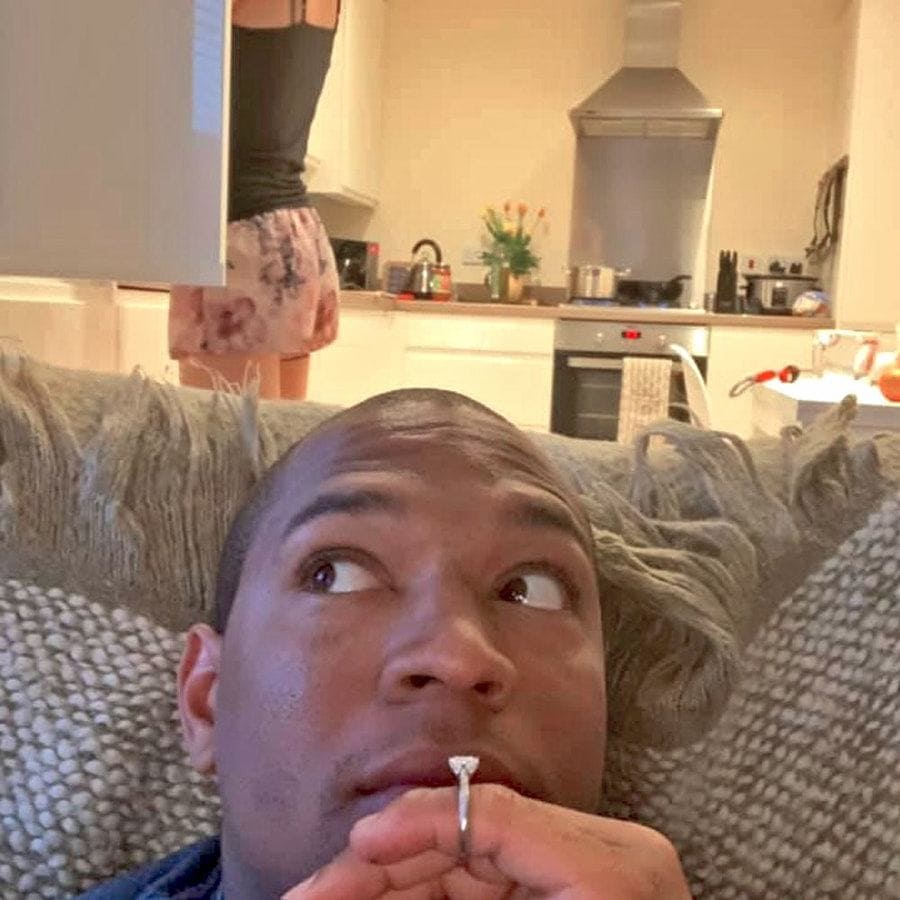 Edi was sitting on the couch with the ring on his finger while Cally looks through a kitchen cabinet behind him.