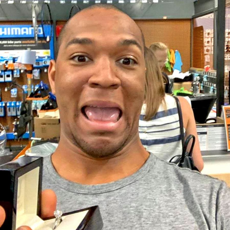 Edi is taking a selfie with the engagement ring in the box and Cally paying at the counter behind him.
