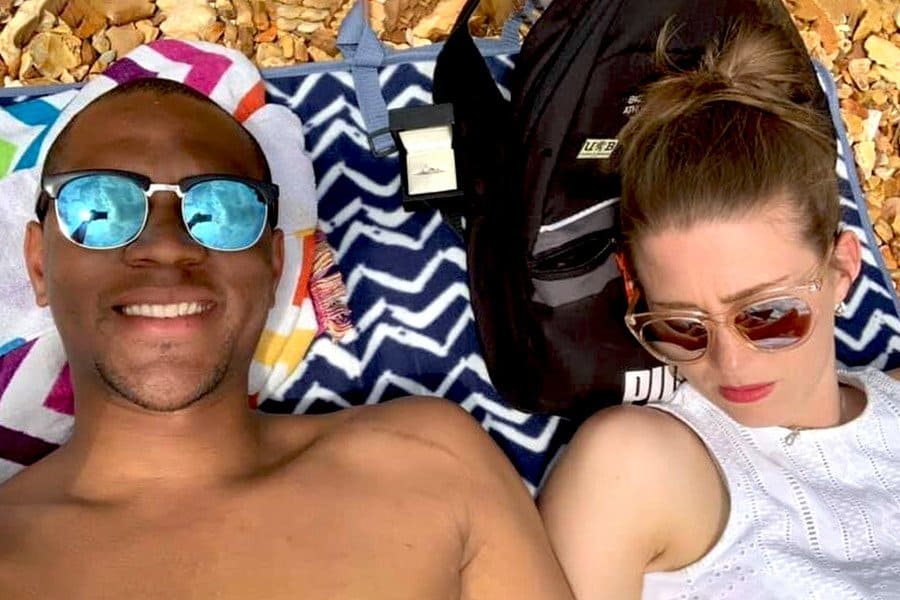 Edi is taking a selfie with the engagement ring while lying next to a sleeping Cally on a beach towel.