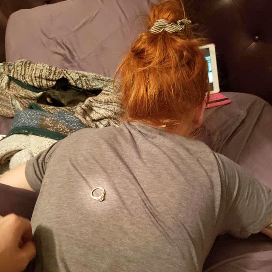 Danielle is lying on the bed stomach down, watching something on her iPad, and Colton has the ring sitting on her back.