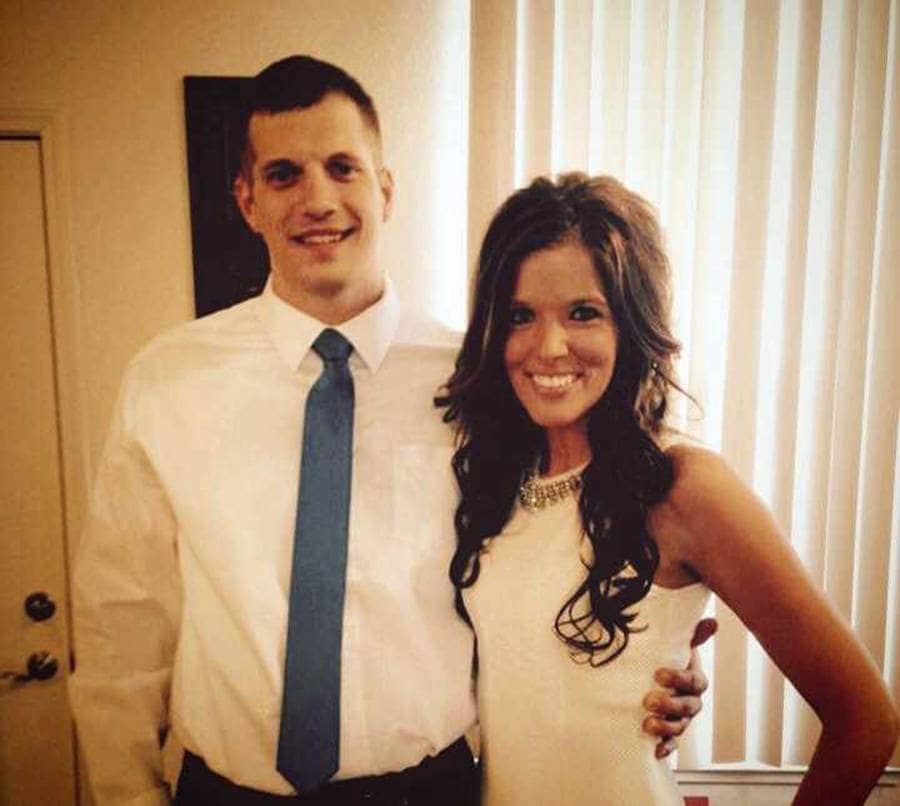 The couple posing, Mandi dressed in a beautiful white dress and Tyler in a button-down shirt with a blue tie.