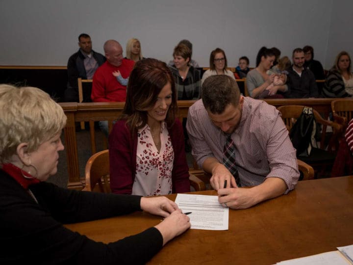 Tyler and Mandi in the courtroom signing a piece of paper.