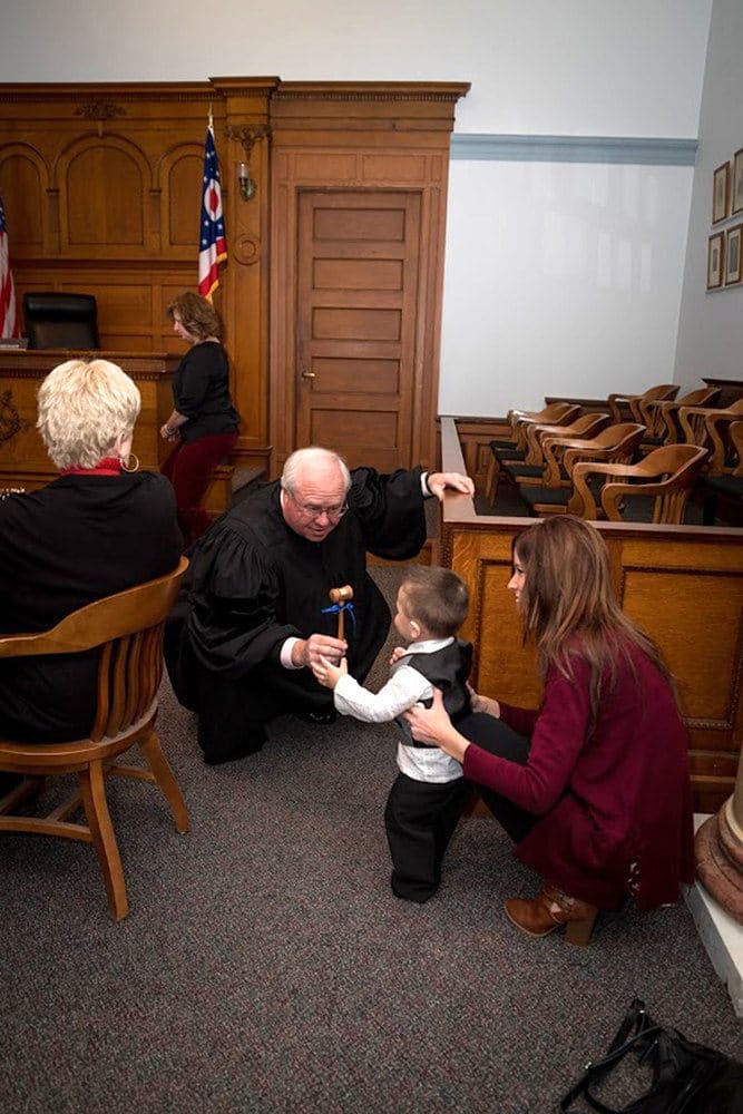 The judge handing hunter a gavel with a blue bow tied around it.