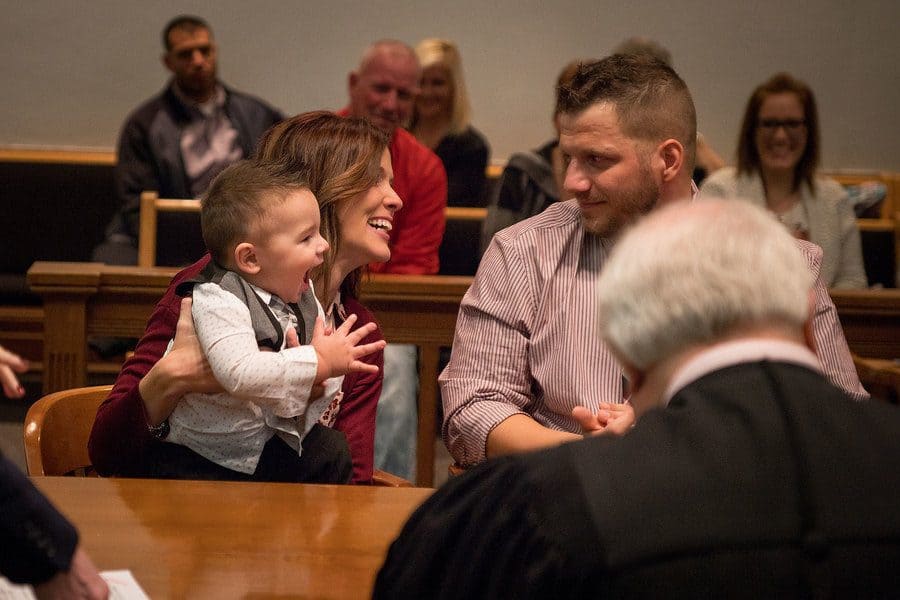 Mandi and Tyler sitting in the courtroom with Hunter clapping and laughing.