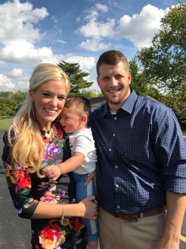 Mandi and Tyler holding Hunter in front of an open area with trees.