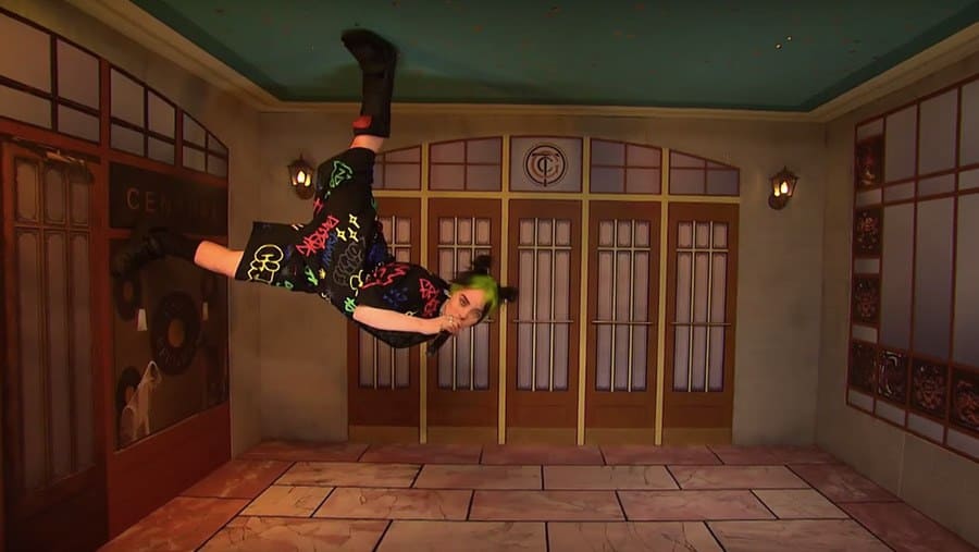 Billie Eilish is seen performing standing on the wall and ceiling on Saturday Night Live. 