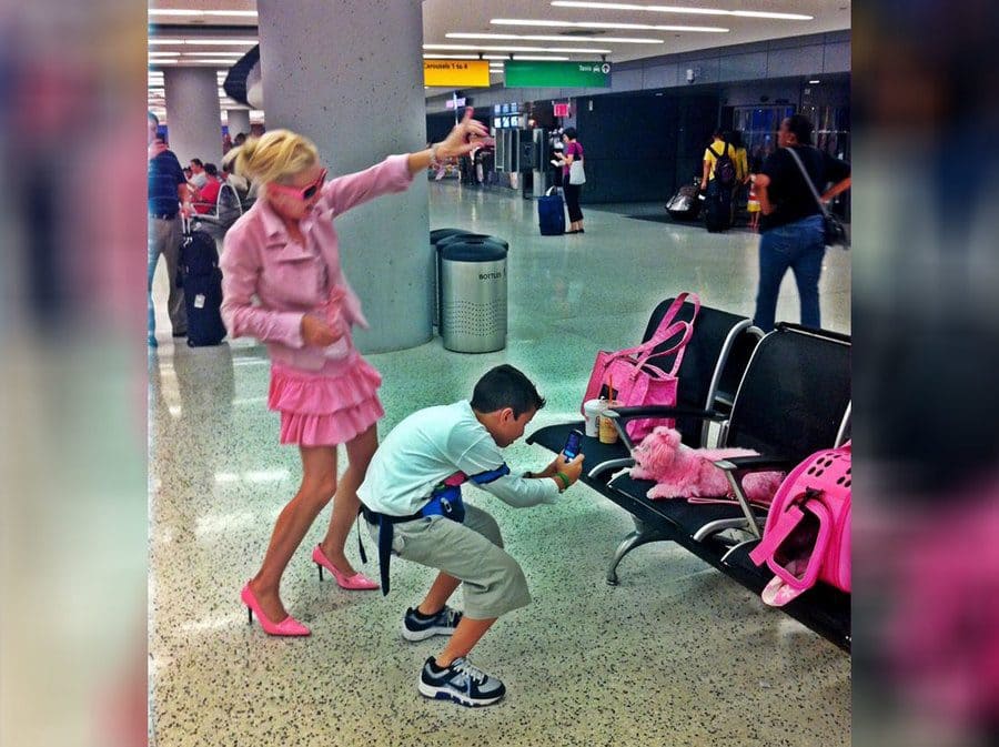 Kitten Kay Sera is in the airport signaling for her pink dog's attention while a fan takes a photograph. 