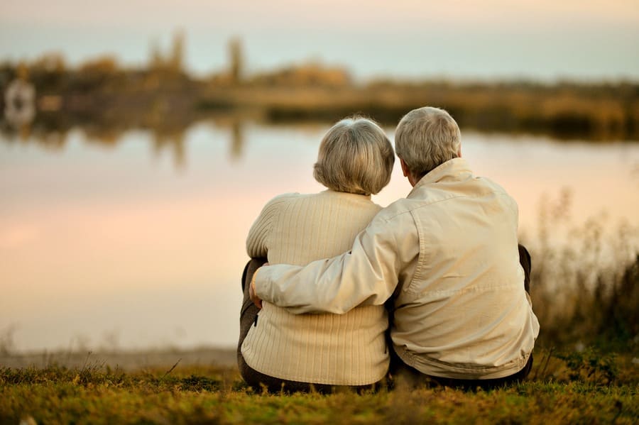 A senior couple sitting by the lake in the summer during the sunset
