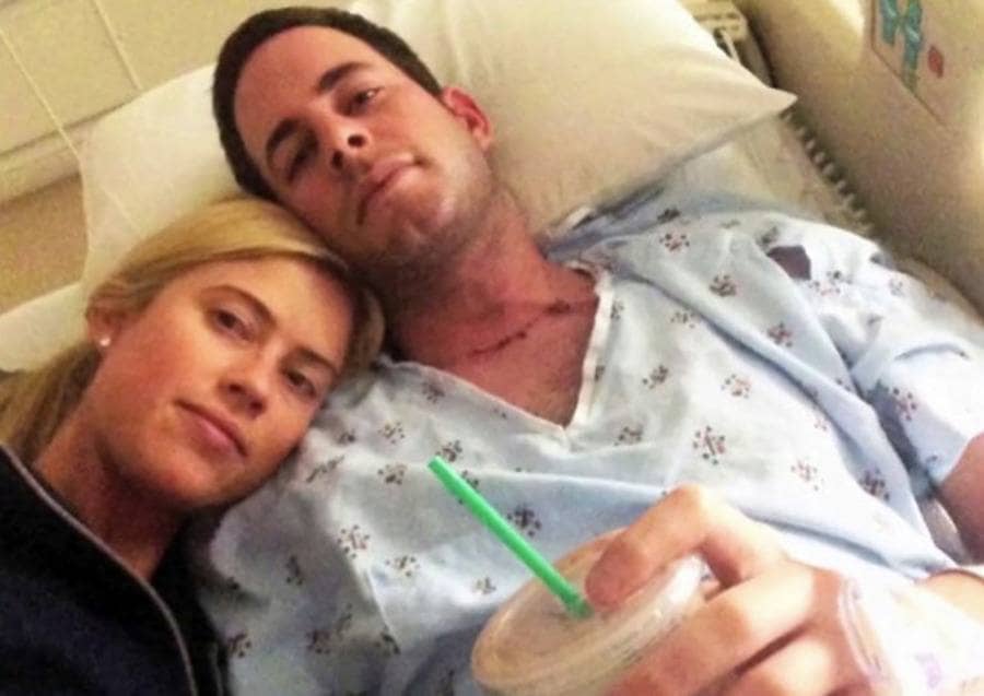 Tarek and Christina are lying next to each other in a hospital bed, and Tarek is holding a coffee. 