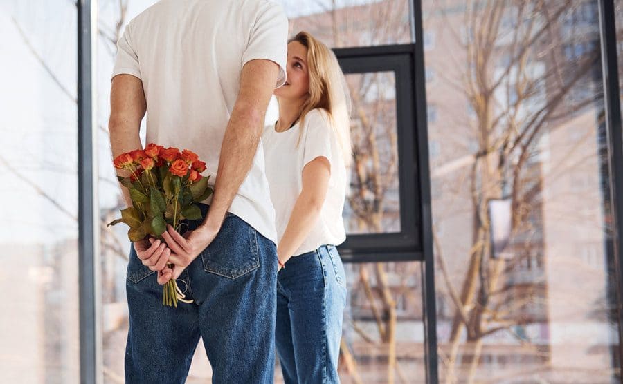 A man holding flowers in his hands behind his back to surprise his girlfriend