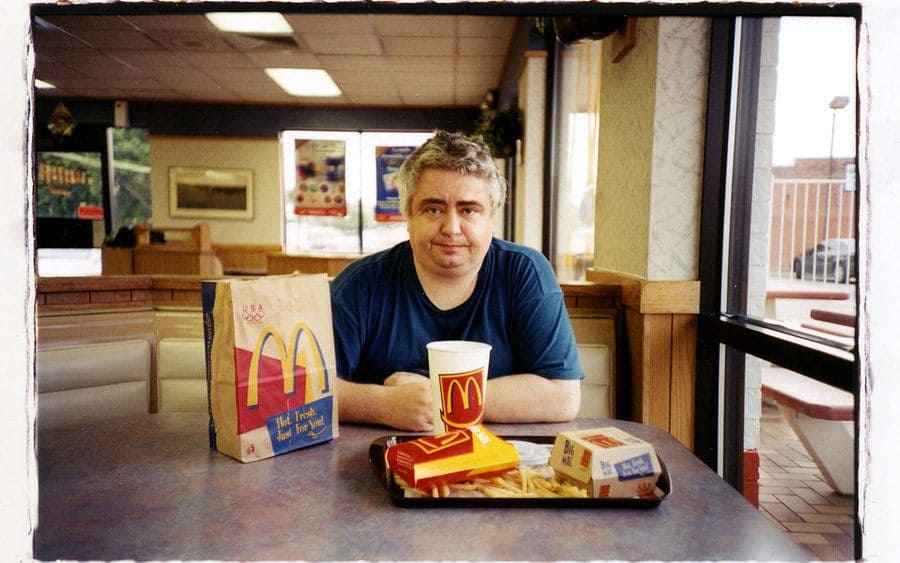 Daniel Johnston sitting down at McDonald's with a meal sitting in front of him 