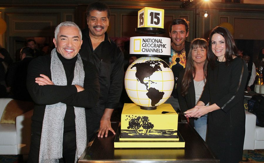 Cesar Millan, Neil deGrasse Tyson, Jason Silva, Sue Aikens, and Courteney Monroe around a large National Geographic three-tiered cake 