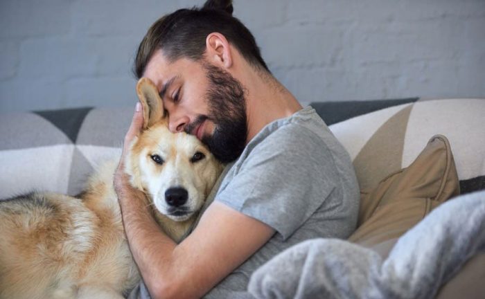 A man is cuddling his dog on the couch. 