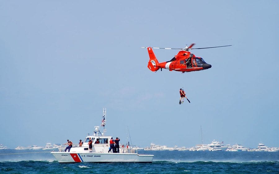 A photograph of a search and rescue mission in the ocean using a helicopter and a boat 