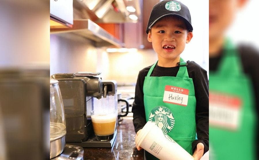 Huxley in his Starbuck’s barista costume with a cappuccino being made in the espresso machine in the family kitchen 