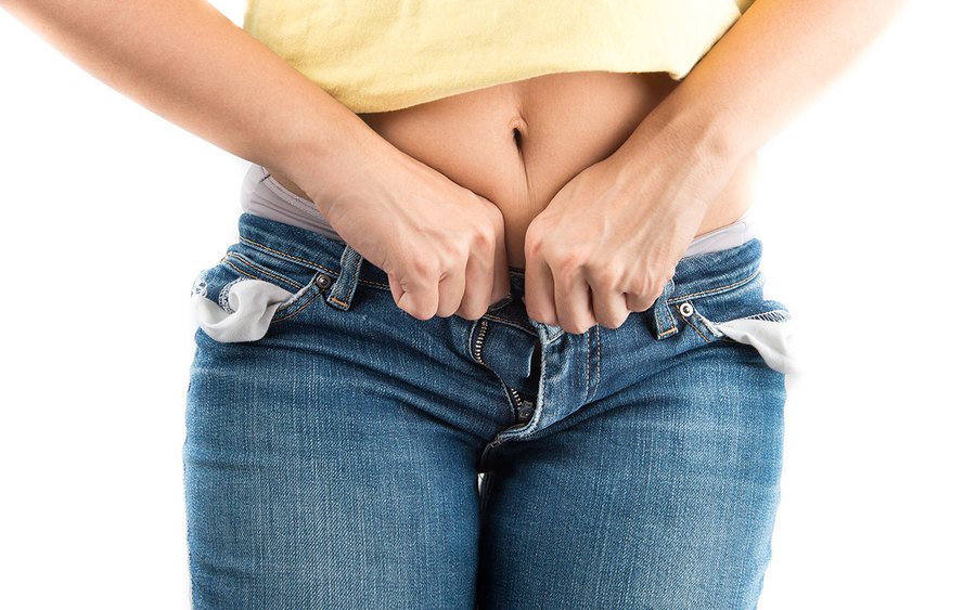 A woman trying to squeeze her jeans shut 