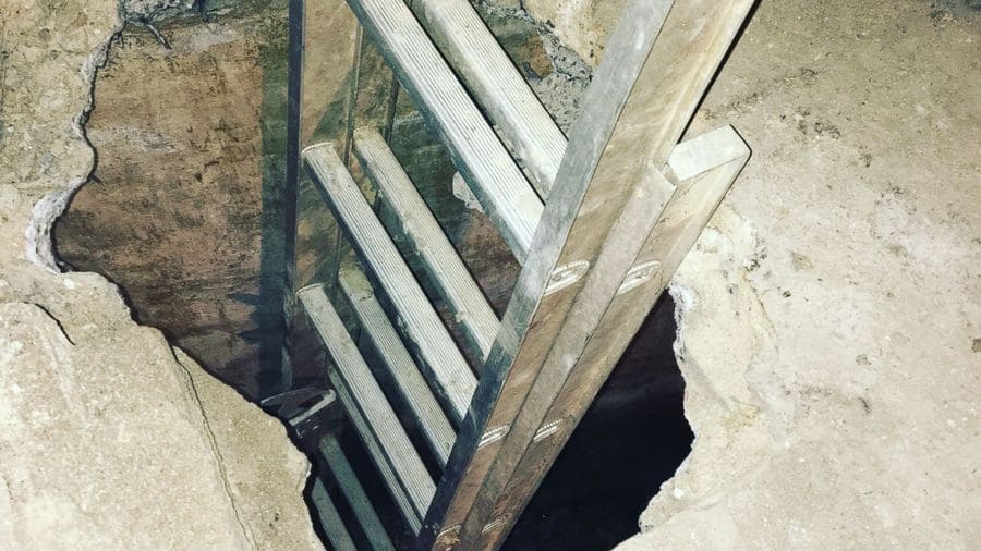 A photograph of a ladder leading underneath a basement floor