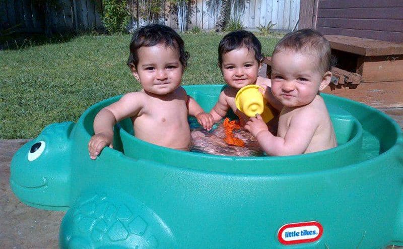 The three girls inside of a little tikes turtle-shaped toy filled with water