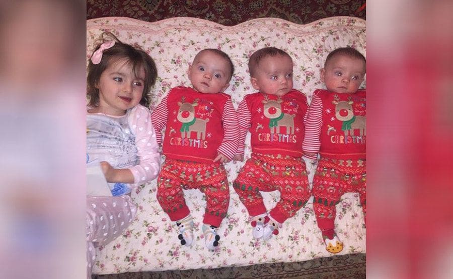 The boys and their sister lying on a floral blanket wearing Christmas sweaters