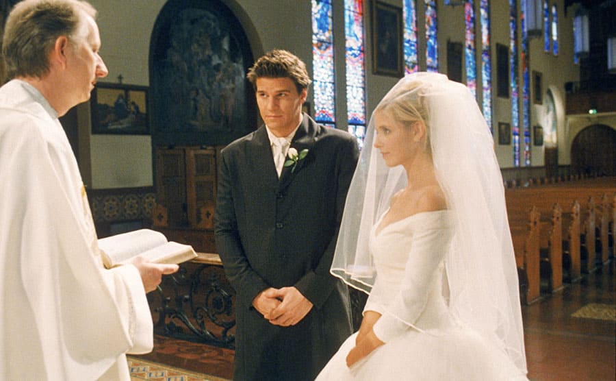 David Boreanaz and Sarah Michelle Gellar standing at alter in front of a Priest