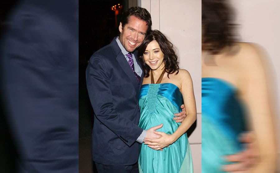 Alyson Hannigan and Alexis Denisof holding her baby bump and smiling 