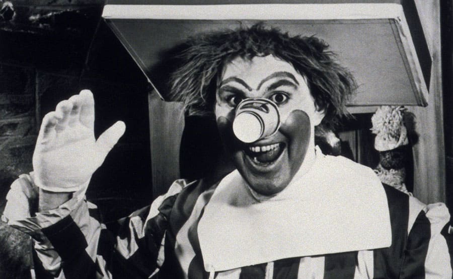 Willard Scott dressed as a clown with a cup on his nose and a meal on a tray which is connected to his belt 