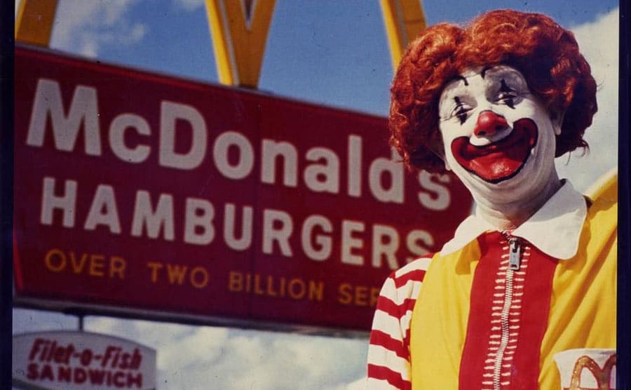 Michael “Coco” Polakovs as Ronald McDonald outside standing in front of a McDonald’s Hamburgers sign