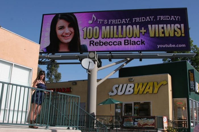 Rebecca black posing next to her billboard 