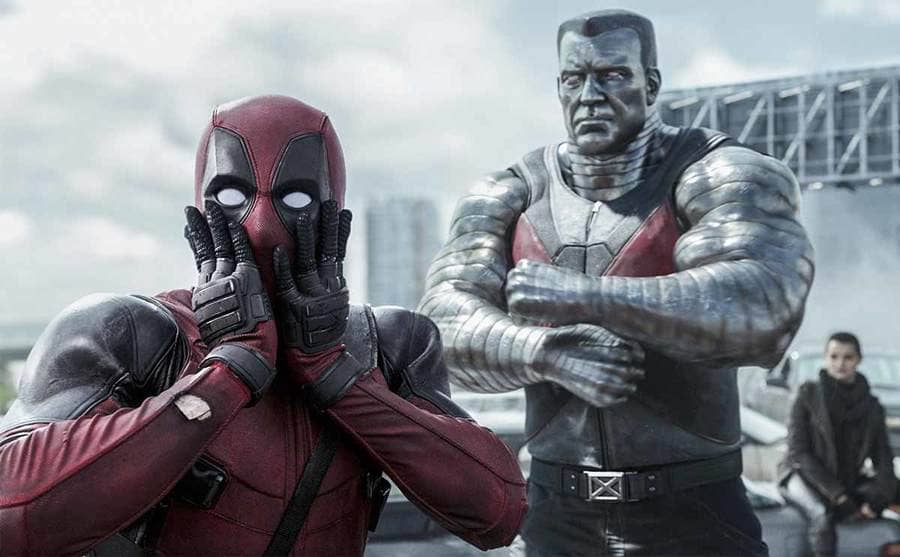 Ryan Reynolds standing shocked with Stefan Kapicic and Brianna Hildebrand behind him in a scene from Deadpool 