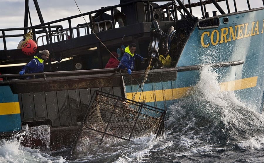The Cornelia crab fishing boat with the crew removing a large cage from the choppy waters 