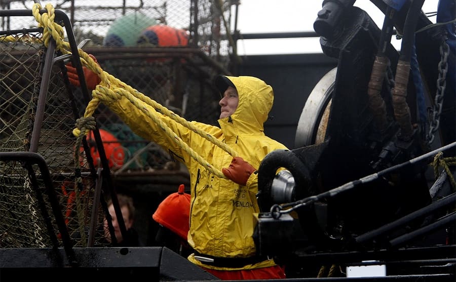 A crew member bringing in a crate of crab wearing a yellow rain jacket on Deadliest Catch 