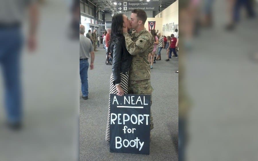 A couple kissing in an airport. The woman holding a sign saying 