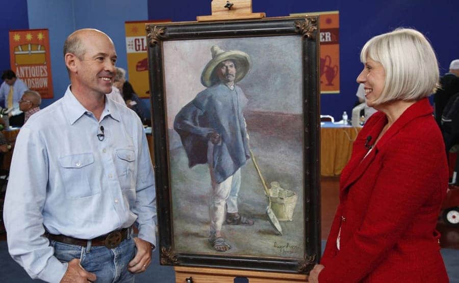 A man with an appraiser looking at an old painting of a man in a flat field 