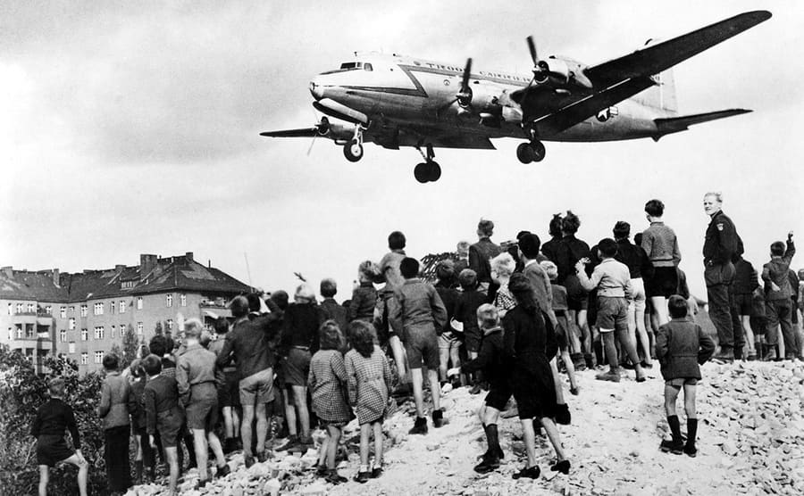 A plane flying above children of Berlin waiting for supplies to be dropped 