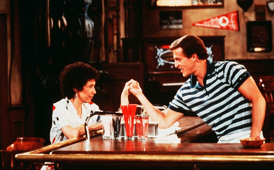 Rhea Perlman and Woody Harrelson showing off their arm strength at the bar on the show Cheers 