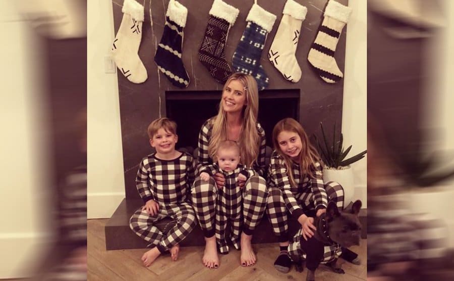 Christina and her kids posing by the fireplace with their dog 